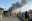 Residents gather along a road as smoke billows after a twin blasts at a market in Parachinar. 