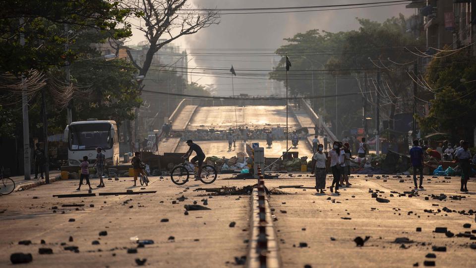 People walk past makeshift barricades set up by protesters to block a road during demonstrations against the military coup in Yangon on March 15, 2021.