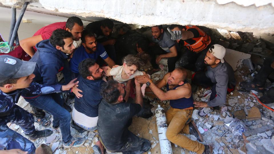 People rescue a wounded child from a debris after Israeli air strikes hit buildings in Al Rimal neighbourhood of main Gaza City, on May 16, 2021.