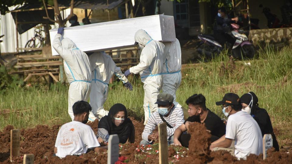 A family gather to grieve at a grave as gravediggers prepare to bury another Covid-19 victim at a cemetary in Bekasi, Indonesia on July 2, 2021.