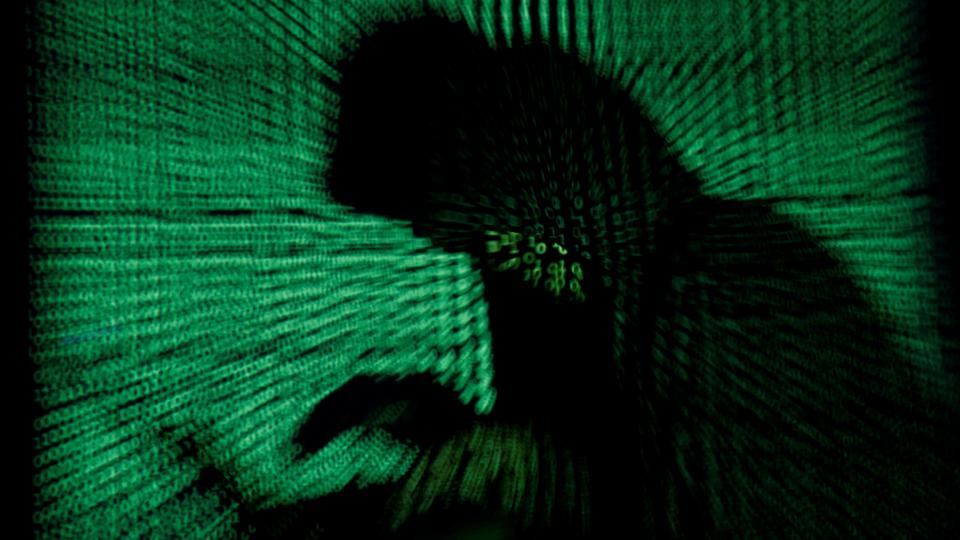 A hooded man holds a laptop computer as cyber code is projected on him in this illustration picture taken on May 13, 2017.