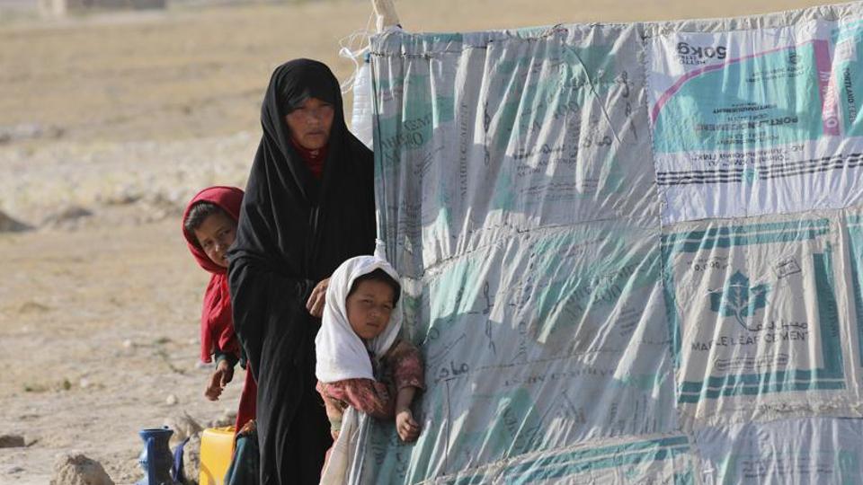 An internally displaced Afghan woman stands with her daughters in front a makeshift tent in a camp on the edge of the city of Mazar-e-Sharif, northern Afghanistan, on July 8, 2021.