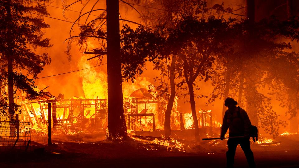 A firefighter passes a burning home as the Dixie Fire flares in Plumas County, California, July 24, 2021.