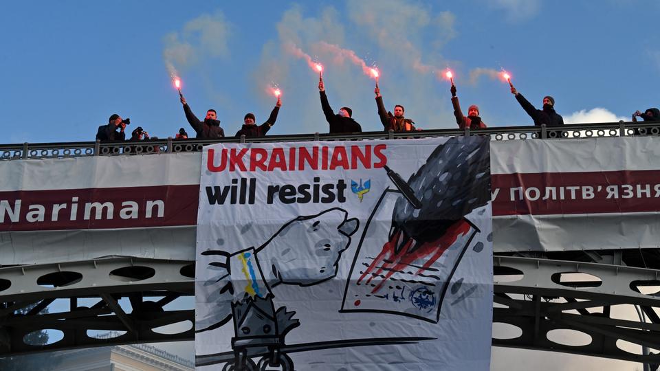 Demonstrators shout slogans as they stand with lit flares on a bridge adorned with a banner 'Ukrainians will resist - Say No to Putin' during a rally in Kiev on February 12, 2022.