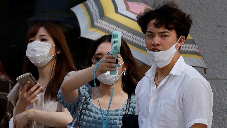 Pedestrians uses a portable fan on the street during a heatwave in Tokyo, Japan, June 27, 2022.