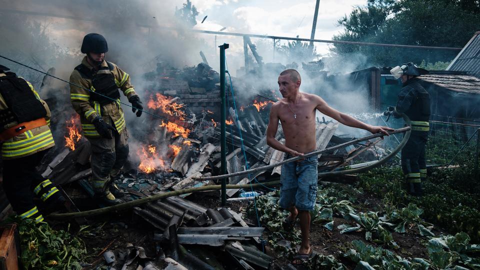 A local resident helps firefighters to put out a fire in a yard of a house in Ukraine's town of Bakhmut following an air strike.