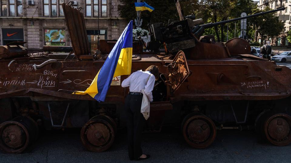 A woman holds the flag of Ukraine while looking into one of the destroyed Russian military vehicles in Kiev.