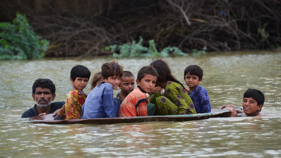 A man (L) along with a youth use a satellite dish to move children across a flooded area in Jaffarabad district of Balochistan province.