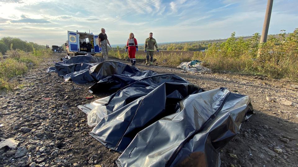 Volunteers stand next to the bodies of killed people at a site of a civilian convoy, which Ukraine says was hit by a shelling of Russian troops in Kharkiv region.