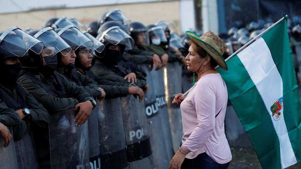 A demonstrator holding a flag stands in front of riot police officers during a protest in Santa Cruz de la Sierra, Bolivia.