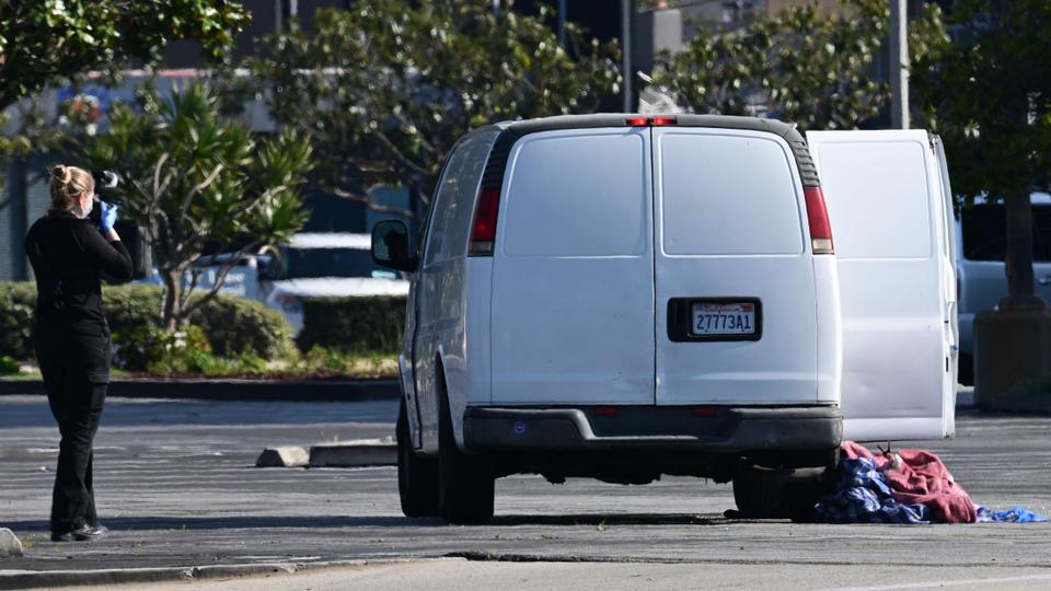 A forensics official takes pictures of a van containing what is believed to be a dead body, as seen in the rearview mirror, in Torrance, California, on January 22, 2023.