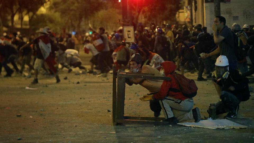 Demonstrators protect themselves with makeshift shields during clashes with riot police in capital Lima,