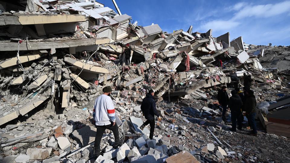 Relatives of victims stand beside the rubble of a collapsed building in the southeastern Turkish city of Kahramanmaras, on February 8, 2023.