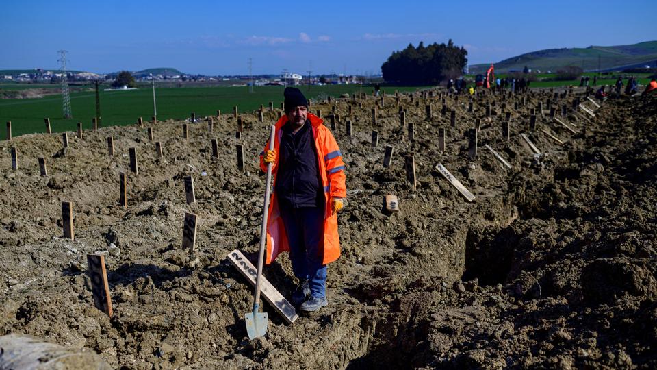 A city employee digs earth in a mass grave area following an earthquake in Hatay, on February 10, 2023.