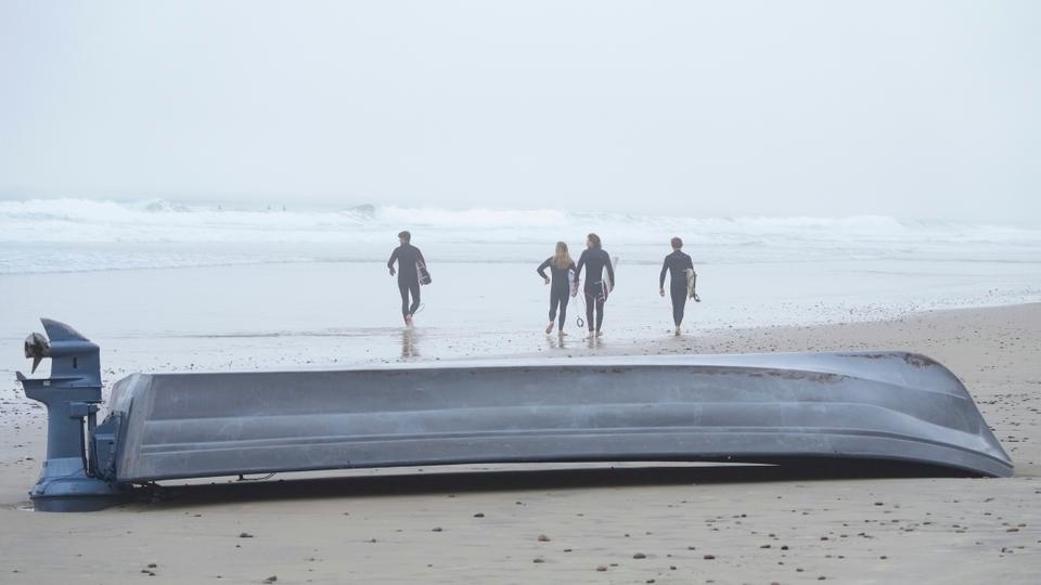 Surfers pass an overturned boat sitting on Blacks Beach in San Diego on Sunday, March 12, 2023.