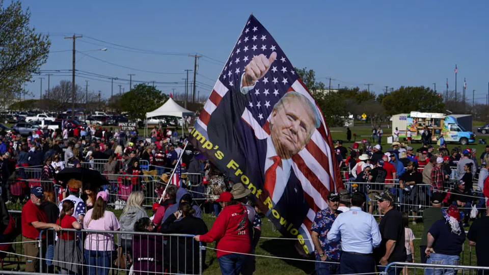 A large flag dons the likeness of Donald Trump as people gather at Waco Regional Airport ahead of Trump's campaign rally.