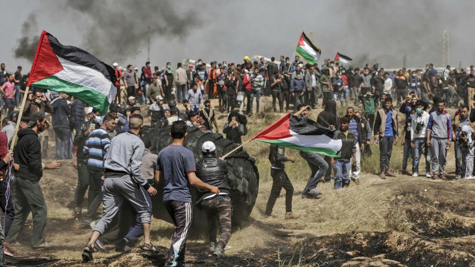 Palestinian protestors wave their national flag as they burn tyres during clashes with Israeli security forces on the Gaza-Israel border following a protest, east of Gaza City on April 6, 2018.