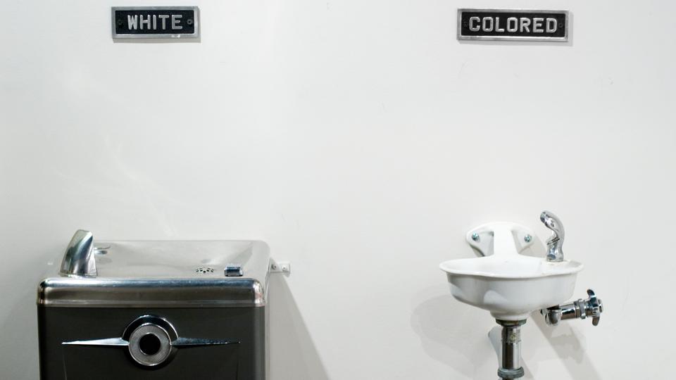 Picture illustrates a segregated water fountain that forced black Americans to drink from a different fountain from those used by US public officers.