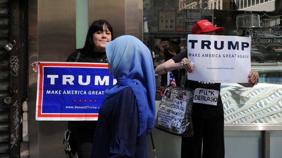 A woman wearing a Muslim headscarf walks past people holding US Republican presidential nominee Donald Trump signs before the start of the annual Muslim Day Parade in the Manhattan borough of New York City, on September 25, 2016.