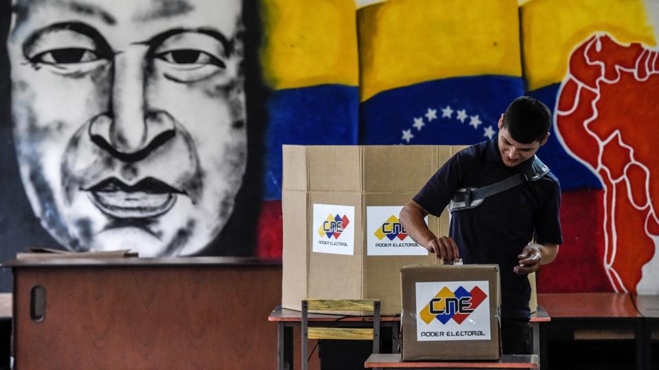 A man casts his vote in front of an image of late Venezuelan president Hugo Chavez, during the presidential elections at a polling station in Caracas on May 20, 2018 .