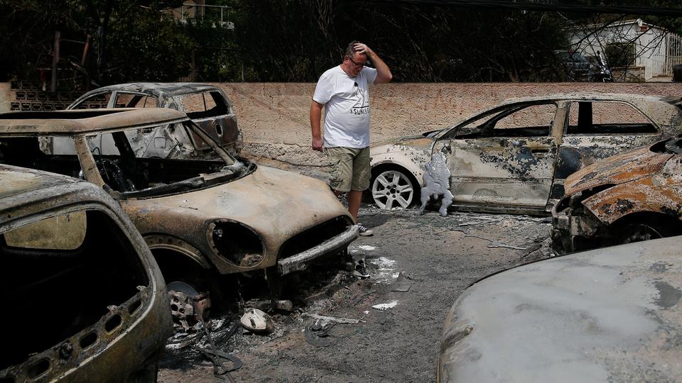 A local reacts as he stands next to burnt cars following a wildfire at the village of Mati, near Athens, Greece, July 24, 2018.