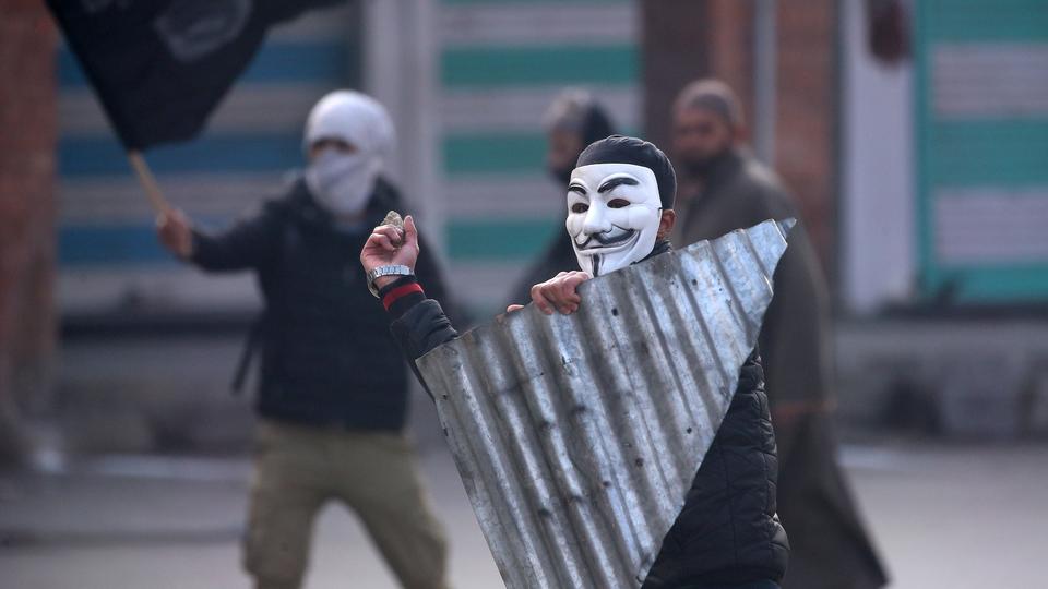 A demonstrator wearing a Guy Fawkes mask throws a stone towards the Indian police (not pictured) during a protest in India-administered Kashmir, Friday, December 14, 2018.