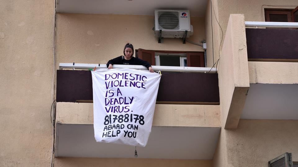 A woman hangs a banner from her balcony with the number of a domestic violence hotline during a national lockdown aimed at stemming the spread of coronavirus, in Beirut, Lebanon, Thursday, April 16, 2020.