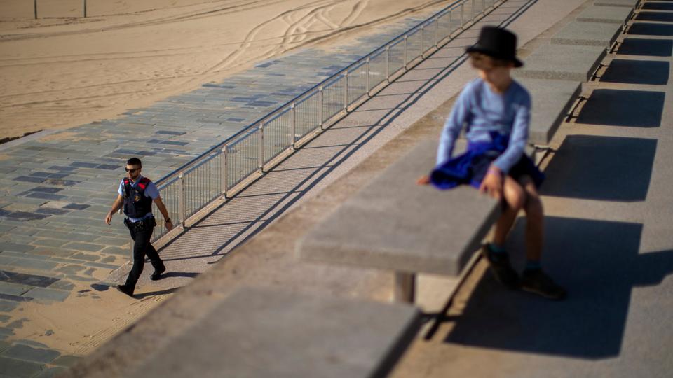 A boy watches as a police officer patrols the beach promenade, where access is prohibited, in Barcelona, ​​Spain, Sunday, April 26, 2020.