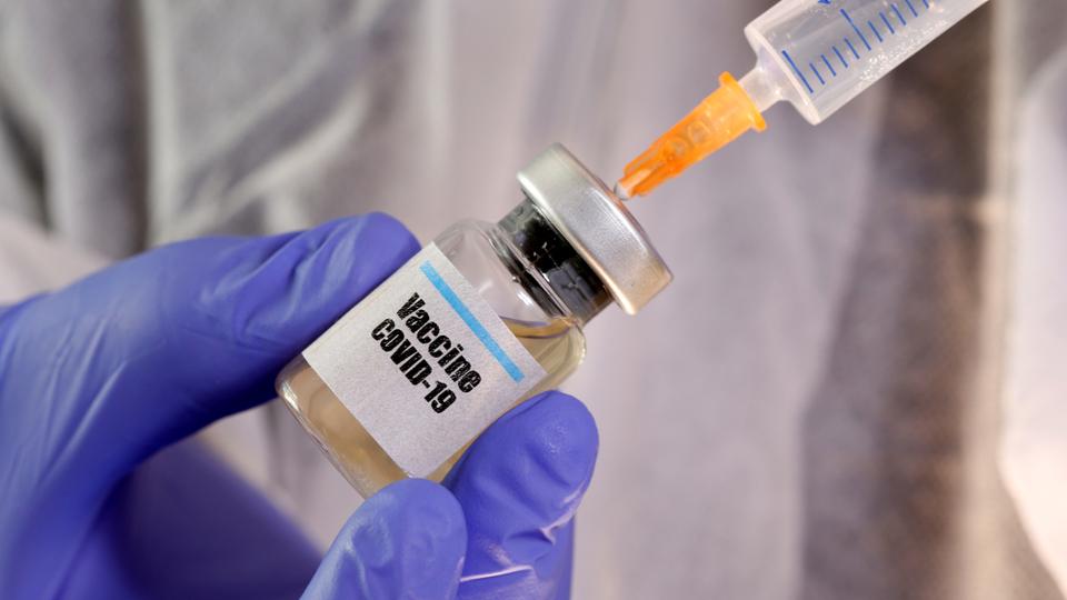 Scientist holding a syringe to bottle filled with a vaccine.