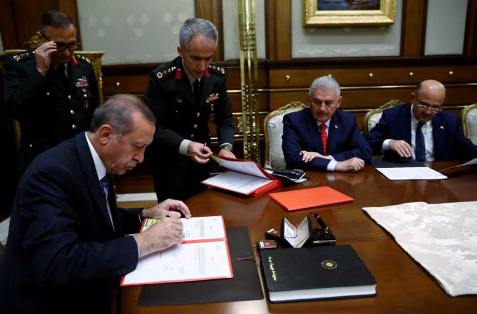 President of Turkey, Recep Tayyip Erdogan (L) signs the decree of the Turkey's Supreme Military Council (YAS) meeting.