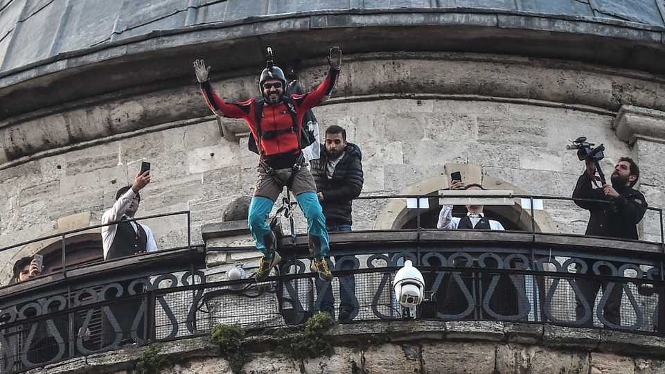 Turkish extreme sports athlete Cengiz Kocak performs a base jump off Galata Tower in Istanbul on November 9, 2017, as part of the events organised by European Outdoor Film Tour (EOFT) in Istanbul.