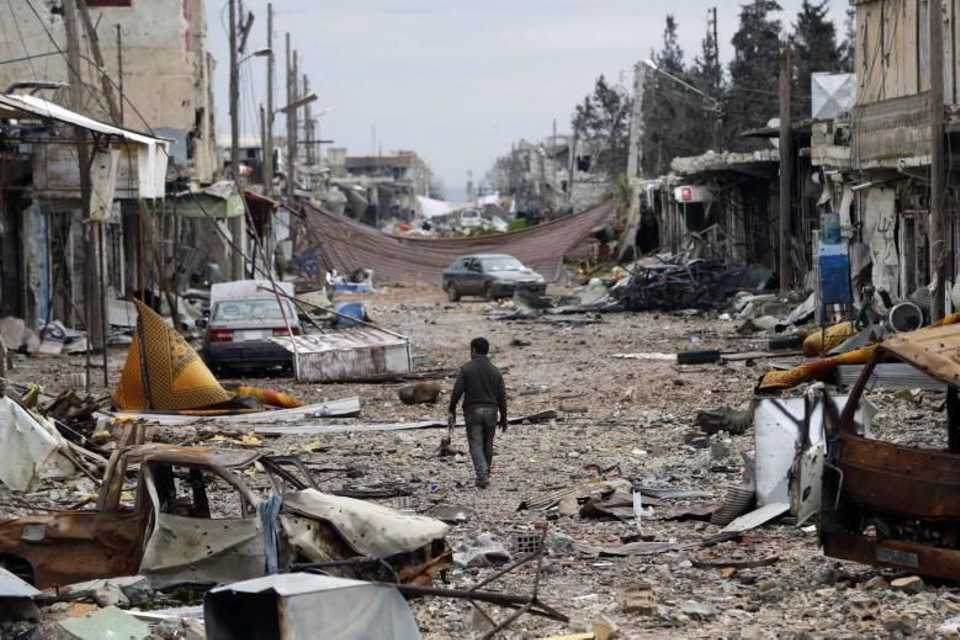 A man walks in a street with abandoned vehicles and and damaged buildings in the northern Syrian town of Kobane on January 30, 2015.