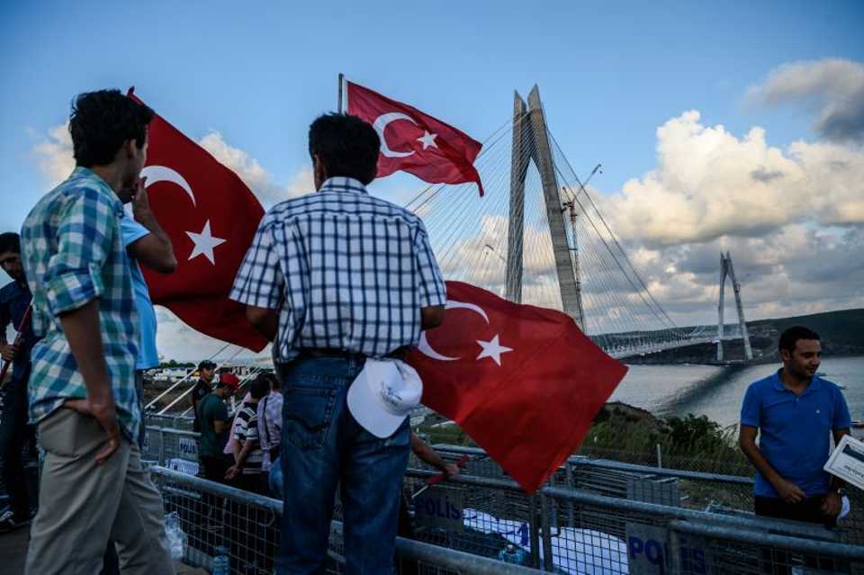 People stand as they hold Turkish national flags next to the Yavuz Sultan Selim bridge on August 26, 2016 in Istanbul during the inauguration of the bridge. 