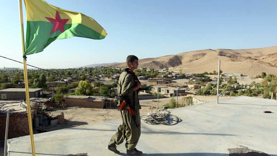 A PKK terrorist walking next to a flag of HPG, an extension of PKK in Sinjar district in northern Iraq.