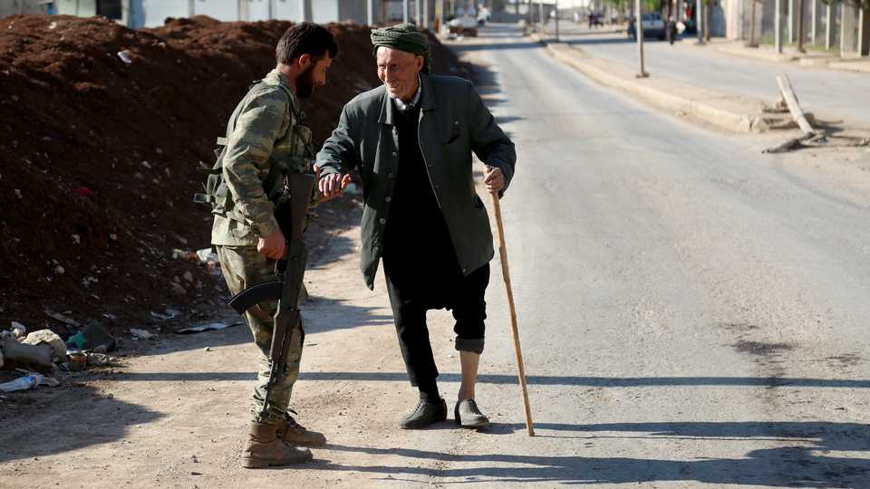 A member of the Free Syrian Army (FSA) helps an old man with walking difficulties at a checkpoint in Afrin, Syria after Turkish Armed Forces and Free Syrian Army (FSA) took complete control of northwestern Syria’s Afrin within the “Operation Olive Branch” on April 01, 2018.