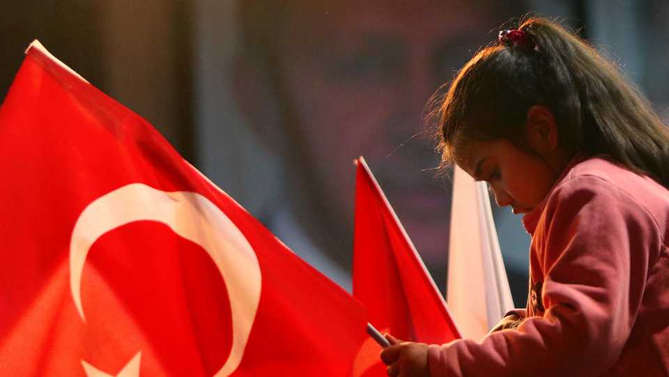 In this March 9, 2017 file photo, a girl holds a Turkish flag as she sits on top of her father in front of a poster of the Turkish President Recep Tayyip Erdogan in the eastern Mediterranean island of Cyprus.