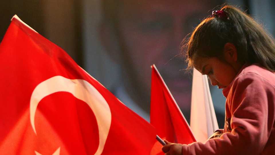 In this March 9, 2017 file photo, a girl hold a Turkish flag as she sit on top of her father as behind seen the poster of the Turkish President Recep Tayyip Erdogan in the eastern Mediterranean island of Cyprus.