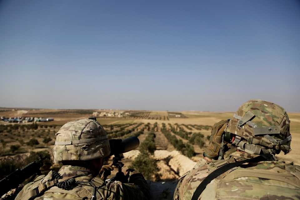 In this February 7, 2018 file photo, American troops look out toward the border with Turkey from a small outpost near the town of Manbij, in northern Syria.