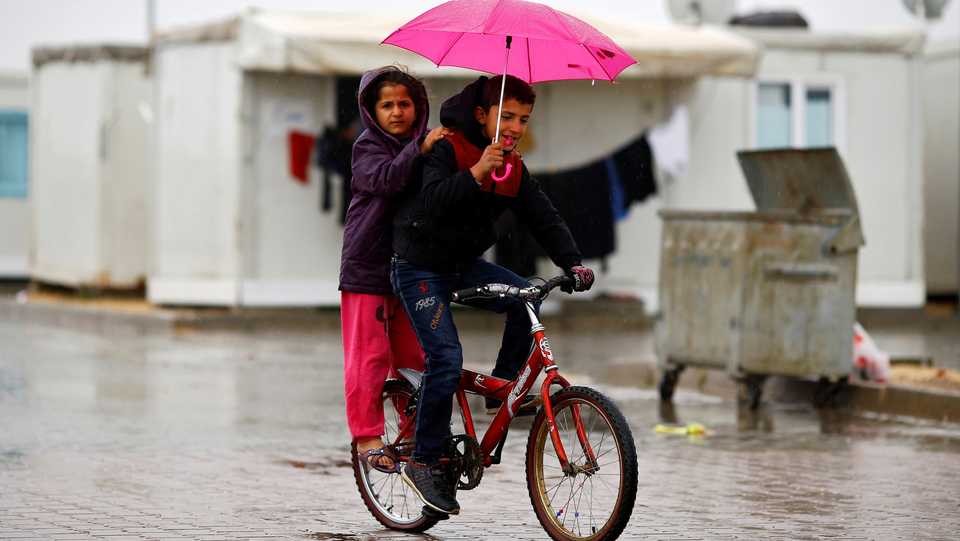 Syrian refugee children ride a bicycle in Elbeyli refugee camp near the Turkish-Syrian border in Kilis province, Turkey, on December 1, 2016.