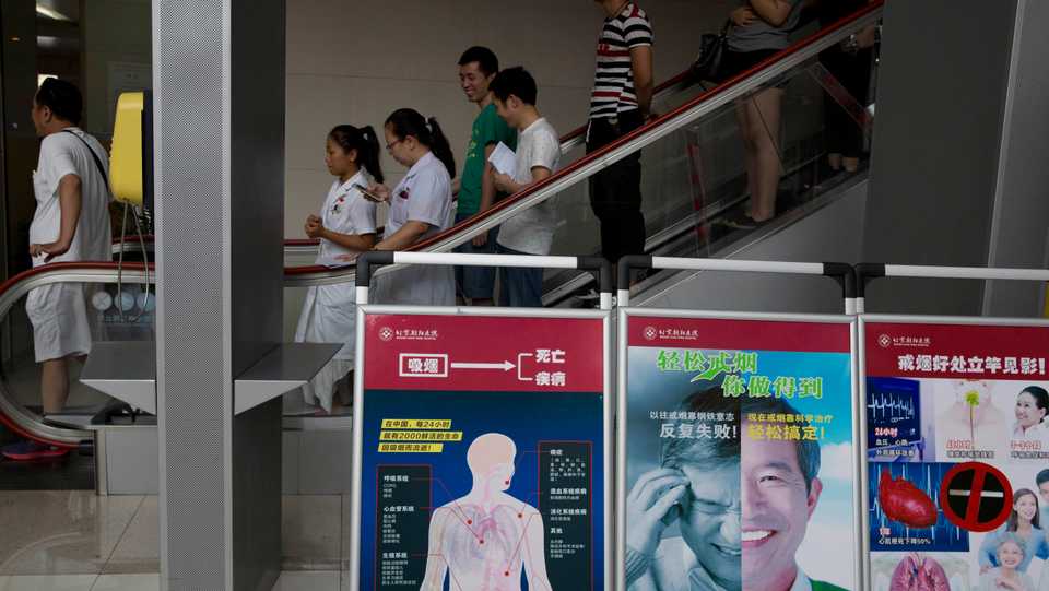 In this photo taken Wednesday, Aug. 24, 2016, hospital staff and visitors pass by boards warning of the damage to human organs from smoking at the Beijing Chaoyang Hospital, one of the hospitals approved for organ transplants, in Beijing, China.