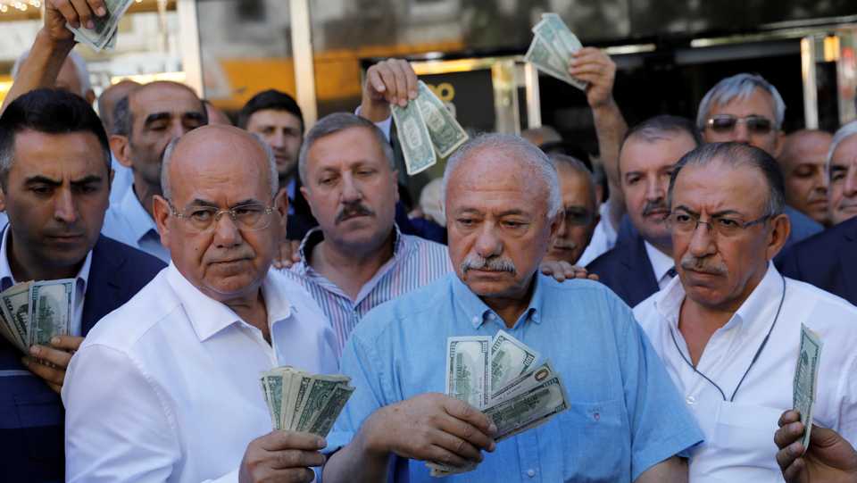 Businessmen holding US dollars stand in front of a currency exchange office in response to the call of Turkish President Erdogan for Turks to sell their dollar and euro savings to support the lira, in Ankara, Turkey August 14, 2018.