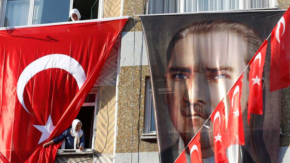 With local elections underway, Turkish people peer out of their windows behind a Turkish flag and a banner of Turkish Republic founder Mustafa Kemal Ataturk.