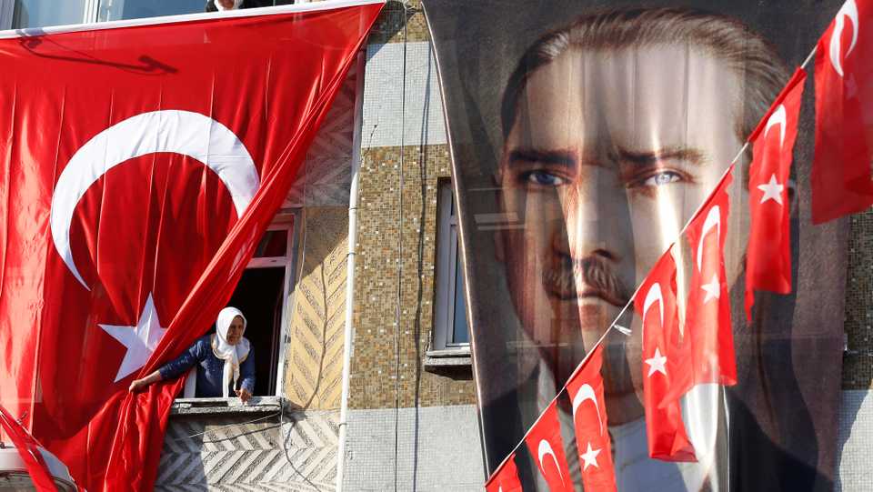 People peer out of their windows behind a Turkish flag and a banner of Turkish Republic founder Mustafa Kemal Ataturk, following a speech of Turkey's President Recep Tayyip Erdogan, at a rally of his governing Justice and Development Party's in Istanbul, Tuesday, March 5, 2019, ahead of local elections scheduled for March 31, 2019.