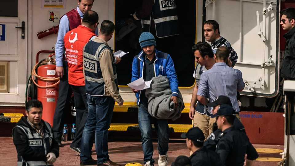 A police officer escorts a refugee from a Turkish ferry, carrying the second group of refugees deported from Europe to the port of Dikili district, Turkey, April 8, 2016.
