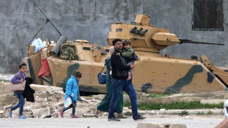A family walks past a military vehicle belonging to Turkish-backed Free Syrian Army fighters after the capture of Khaldieh village, in eastern Afrin, Syria on March 10,2018.