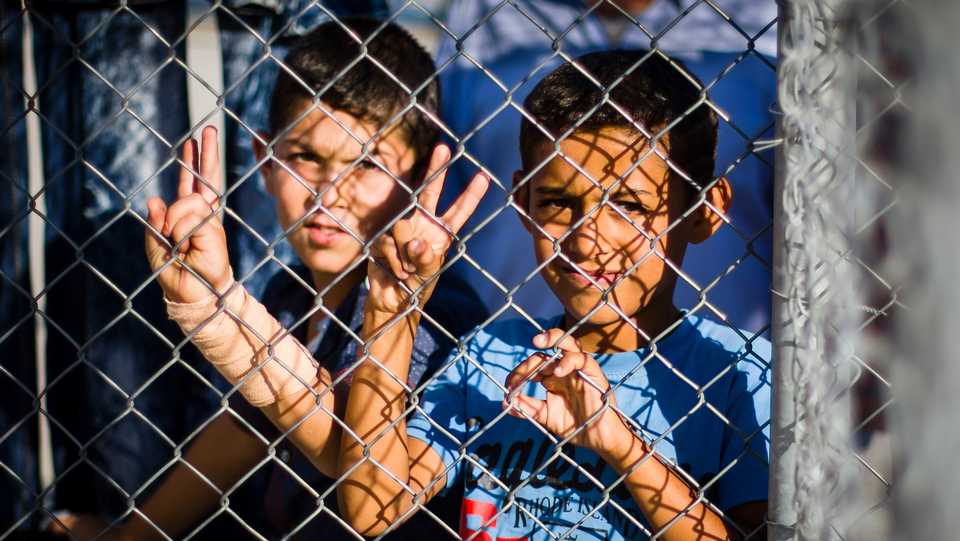 Two Syrian refugee children stand behind a fence in an AFAD refugee camp and show the Peace symbol on October 07, 2016 in Nizip, Turkey.