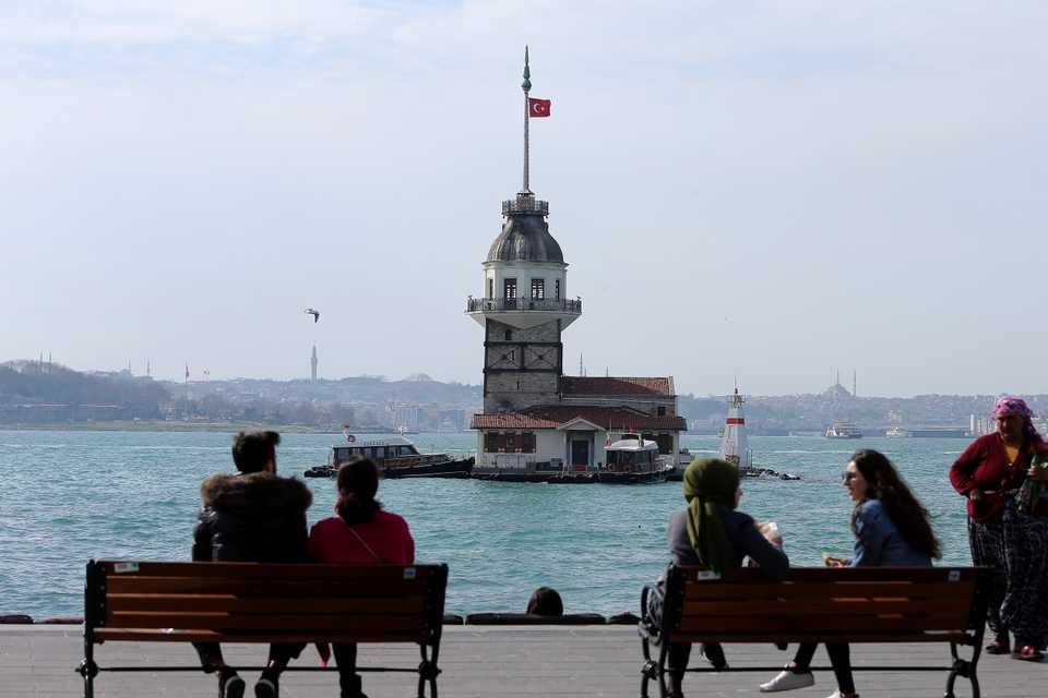 Maiden's Tower is seen as people have a talk and take a walk at Salacak beach during a sunny day in Istanbul, Turkey on March 01, 2019.