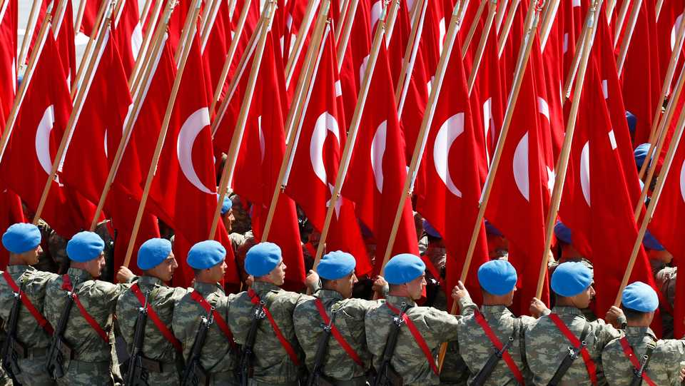 Turkish soldiers carry Turkish flags during a parade.