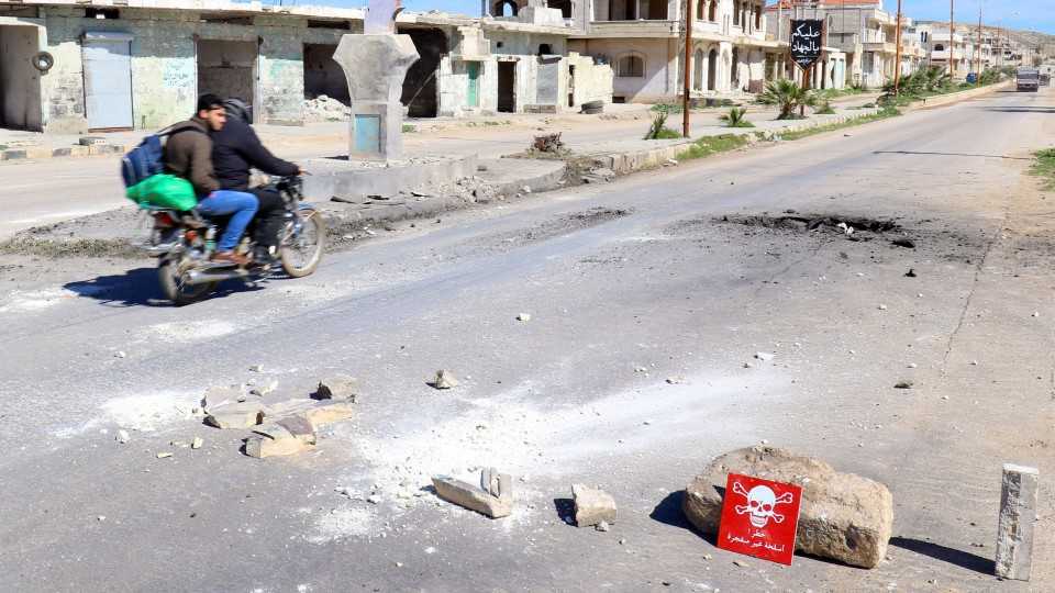Men ride a motorbike past a hazard sign at a site hit by an airstrike on Tuesday in the town of Khan Sheikhoun in rebel-held Idlib, Syria April 5, 2017. The hazard sign reads, "Danger, unexploded ammunition".