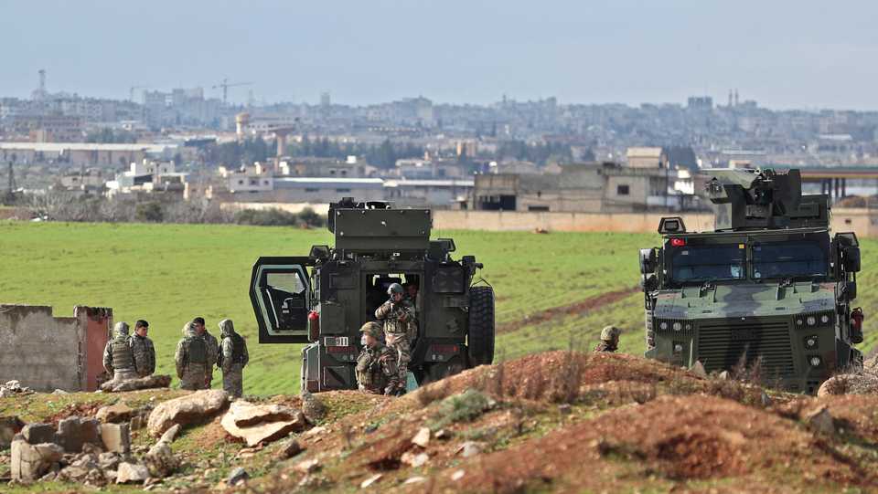 A Turkish soldier looks through the scope of his rifle as others gather by military vehicles at a Turkish observation point near Sarmin on the outskirts of the city of Idlib in the northwestern Syrian Idlib province on February 7, 2020.